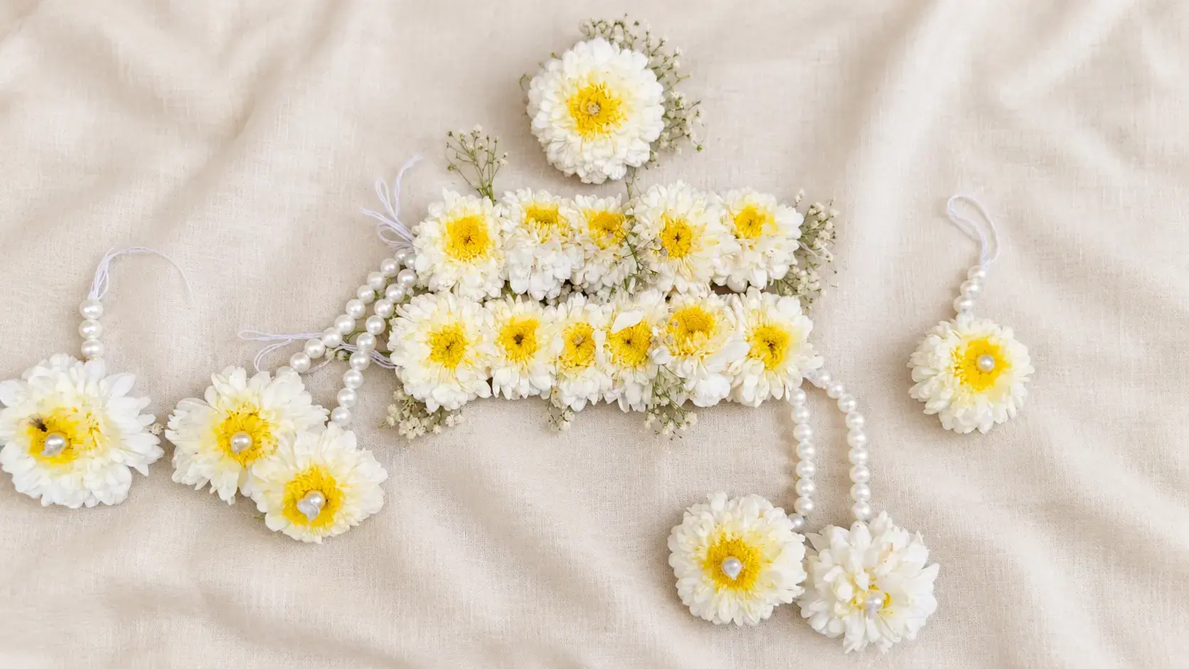 White and yellow guldavri floral jewellery set with pearl-style bead strands on ivory fabric.