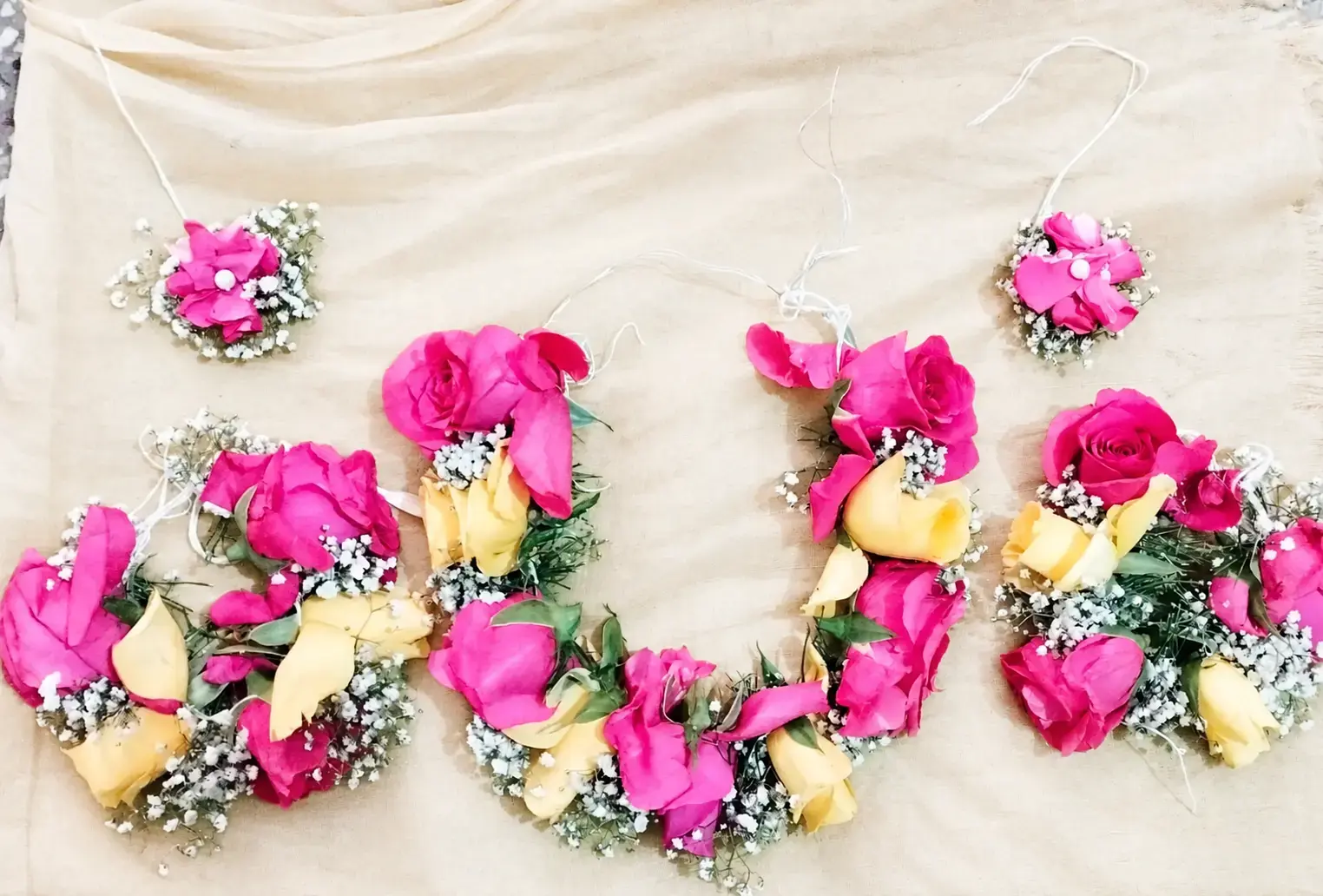 Pink and yellow rose floral jewellery set with white filler flowers arranged on ivory fabric.